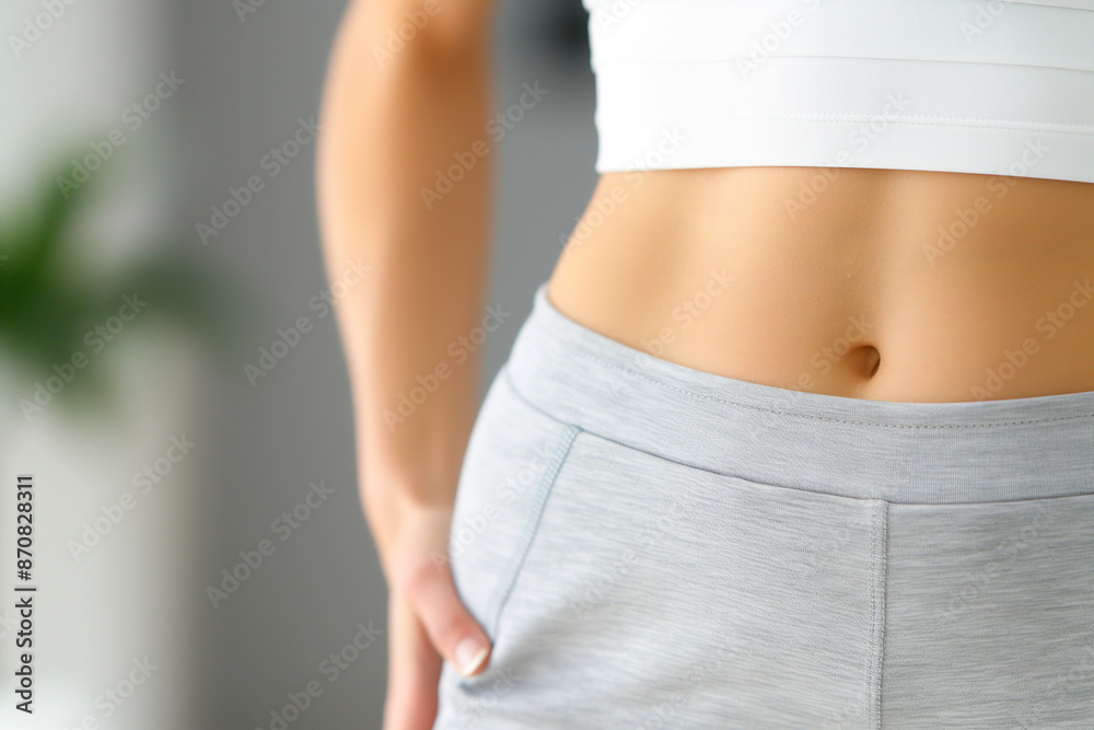 Fototapeta premium Close up of a woman's waist and belly, showing a slim body shape after weight loss or fitness training while wearing white sportswear.