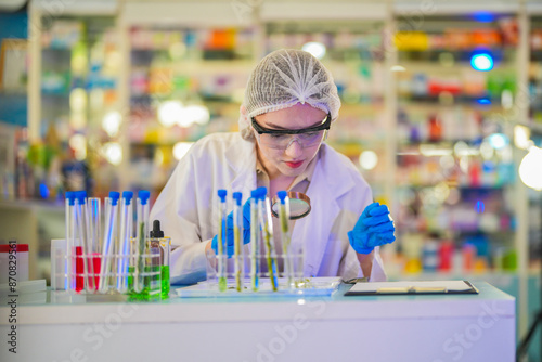 female scientist Experimenting through tubes of chemical liquids and plant samples. In a laboratory with test samples in the background in a modern laboratory By testing safely and cleanly.