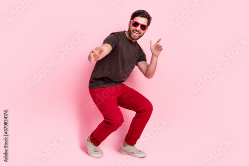Full size photo of handsome man with stylish bristle dressed brown t-shirt in sunglass indicating at you isolated on pink color background © deagreez