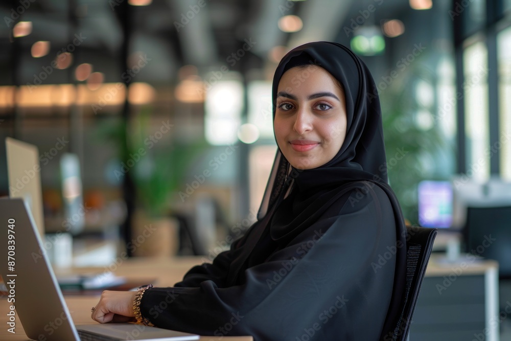 Happy Arab woman in abaya looking at front camera with laptop computer Blurred notebook and office