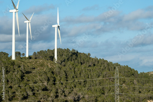 Three wind turbines are seen among dense forest trees on a sunny hillside, representing the development of technology harmonizing with natural environments. photo