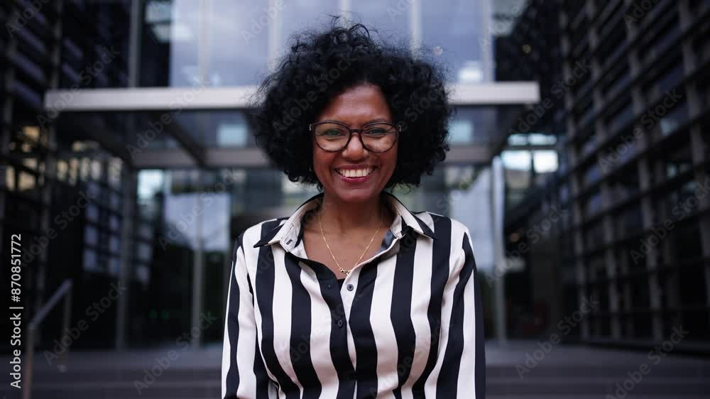 Camera zoom of adult African American business woman posing smiling standing with hands clasped together in front office building. Cheerful and empowered black female looking happy at camera outdoors
