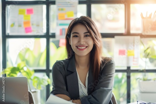 Smiling businesswoman sitting at her desk with arms crossed in a modern office.  She is looking at the camera with a confident expression.