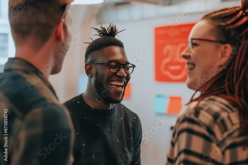 Three colleagues laughing and talking together in a casual office setting.