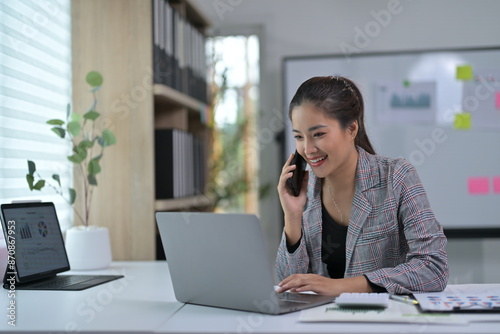 Young Professional Woman Working on Laptop and Talking on Phone in Modern Office Environment