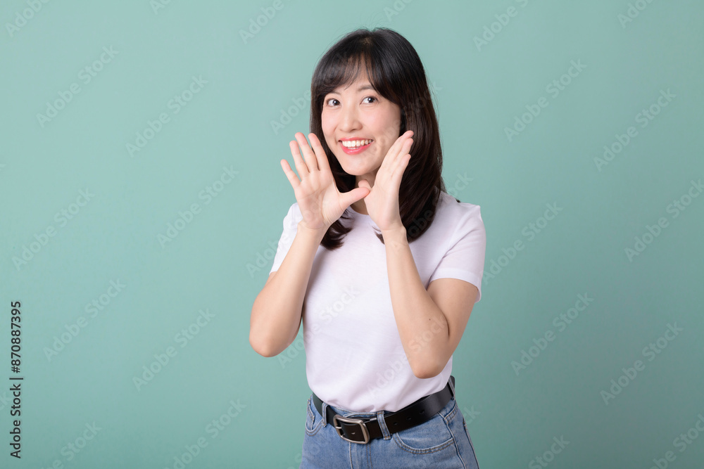 Smiling positive, asian young woman holding hands near mouth, expressing excitement, isolated on green. Smiling positive, asian young woman holding hands near mouth, expressing excitement, isolated on green.