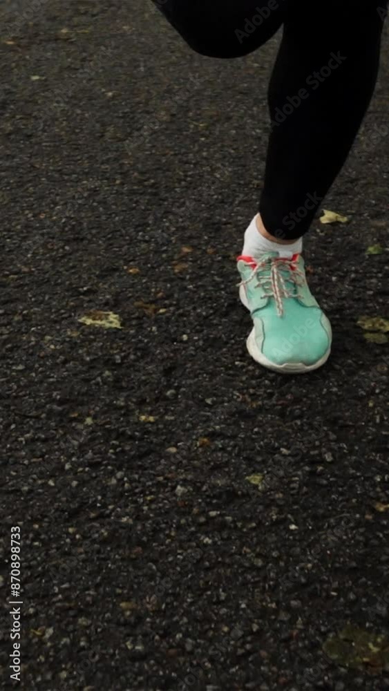 Woman runner boots sneakers in super slow motion in the park on asphalt park forest road close-up Vertical shot. Woman runner boots sneakers in super slow motion in the park on asphalt park forest road close-up Vertical shot.