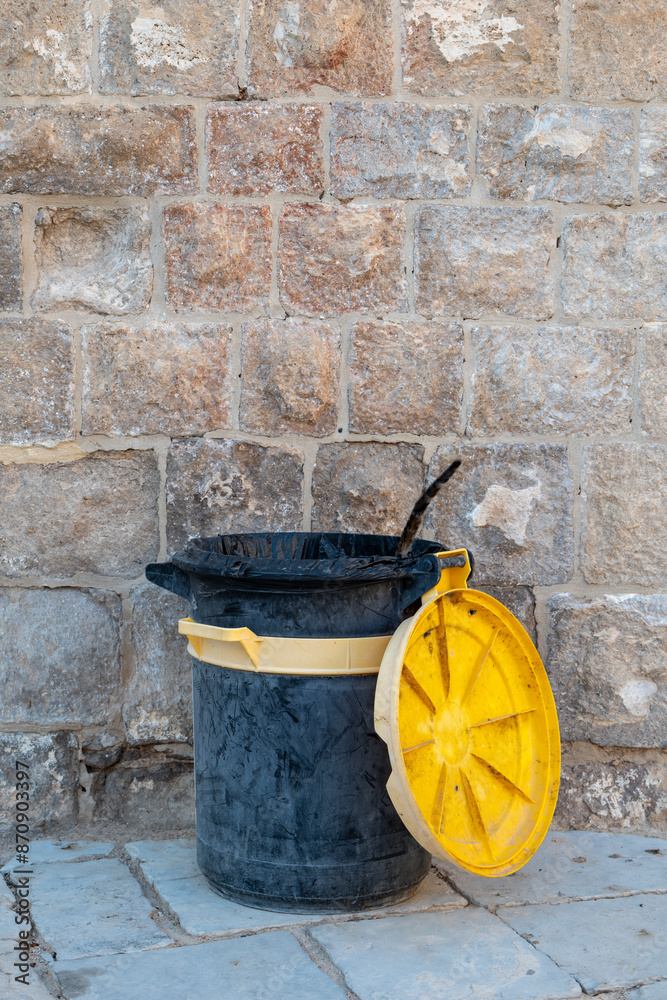 Tail of a Cat Appears Out From a Black and Yellow Plastic Garbage Can