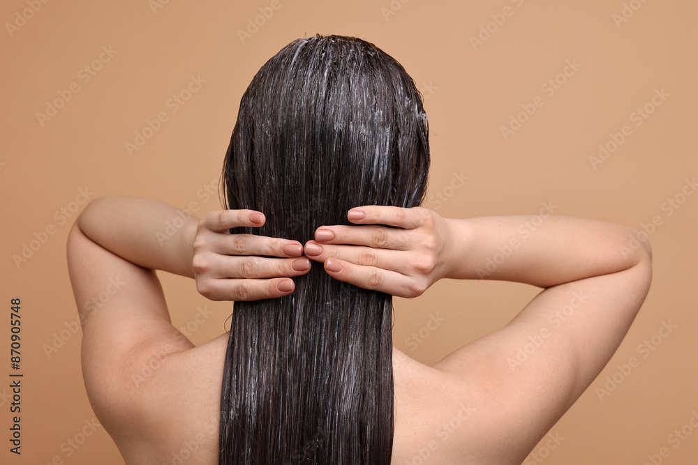 Naklejka premium Woman applying hair mask on beige background, back view