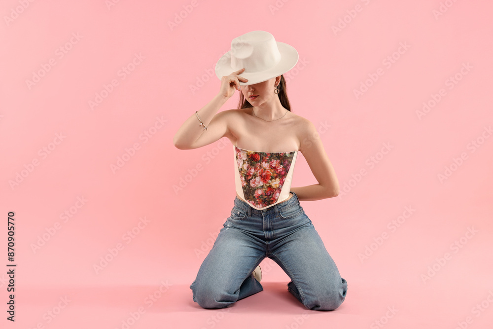 Woman in stylish corset covering eyes with hat on pink background Woman in stylish corset covering eyes with hat on pink background