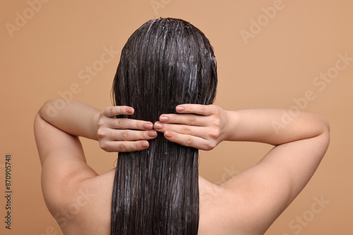 Woman applying hair mask on beige background, back view