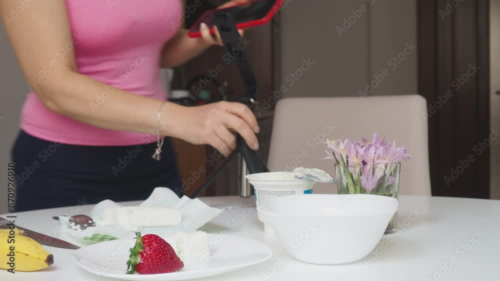 girl blogger films breakfast for video blog, content for social networks, stories. Hands with the phone close-up pictures of food. Breakfast for two : yogurt, coffee, fruit , toast., strawberry, banan