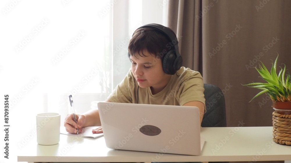 boy, teenager, schoolboy, wearing headphones, uses a laptop and communicates on the Internet at home. homeschooling, distance learning, online e. Watches videos, communicates on social networks, makes boy, teenager, schoolboy, wearing headphones, uses a laptop and communicates on the Internet at home. homeschooling, distance learning, online e. Watches videos, communicates on social networks, makes