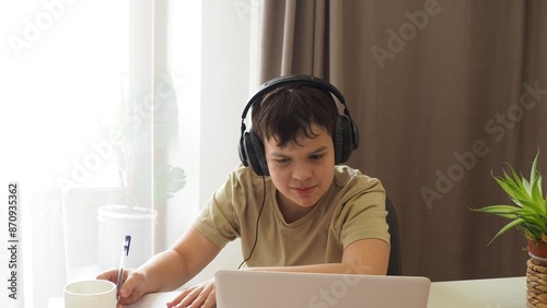boy, teenager, schoolboy, wearing headphones, uses a laptop and communicates on the Internet at home. homeschooling, distance learning, online e. Watches videos, communicates on social networks, makes
