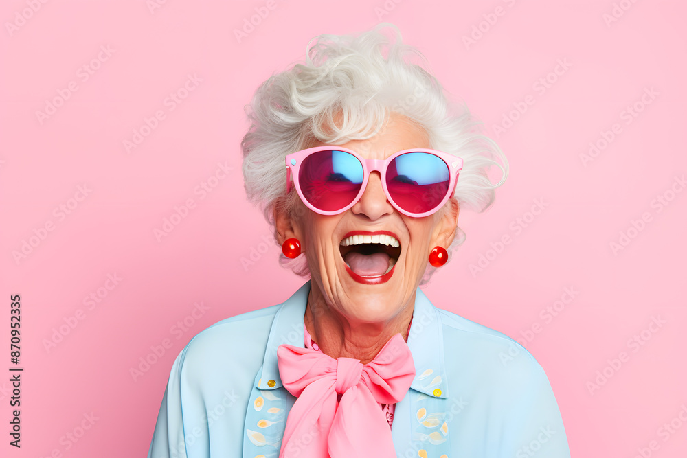 Elderly woman laughing joyfully, wearing stylish sunglasses, colorful attire, against a pink background. Fun and lively senior portrait.