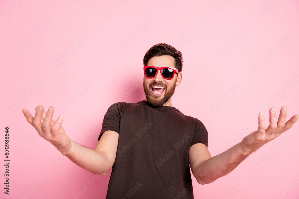 Photo of ecstatic man with stylish bristle dressed brown t-shirt in sunglass hands hold empty sapce isolated on pink color background Photo of ecstatic man with stylish bristle dressed brown t-shirt in sunglass hands hold empty sapce isolated on pink color background
