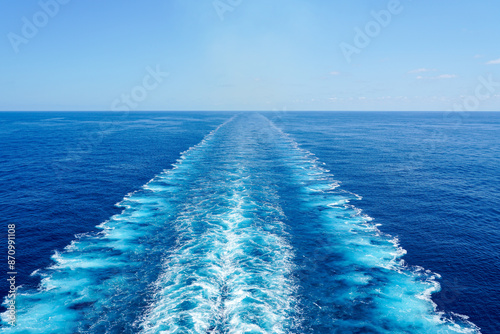 Wide turbulent white foam water trail behind a large cruise ship in a calm blue sea on a sunny day
