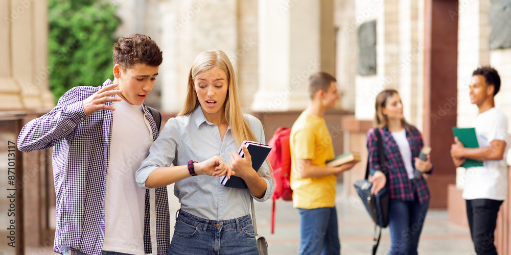 Fototapeta premium Shocked students in university campus looking at watches, being late for classes, copy space