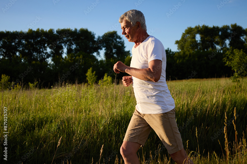Senior man with silver hair running in the rural area engaging in outdoor exercise to maintain his health jogging on bright summer morning Senior man with silver hair running in the rural area engaging in outdoor exercise to maintain his health jogging on bright summer morning