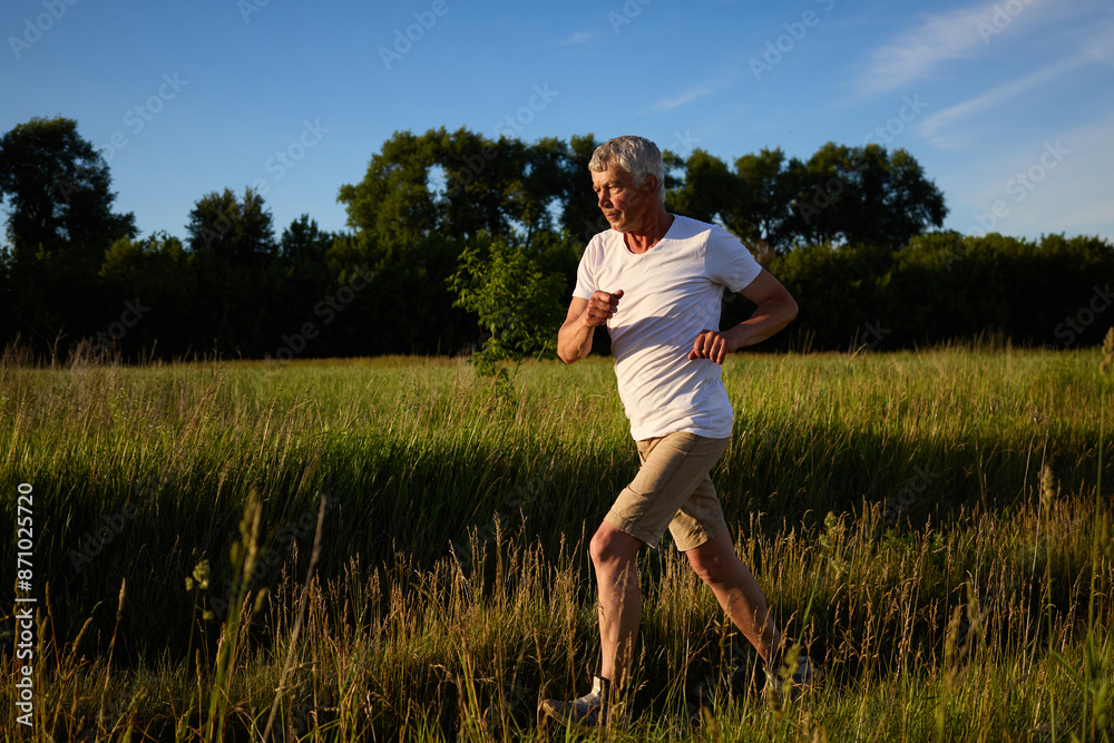 Mature gray haired man jogging in countryside doing sport exercising in open air taking care of his health running in sunny summer morning Mature gray haired man jogging in countryside doing sport exercising in open air taking care of his health running in sunny summer morning
