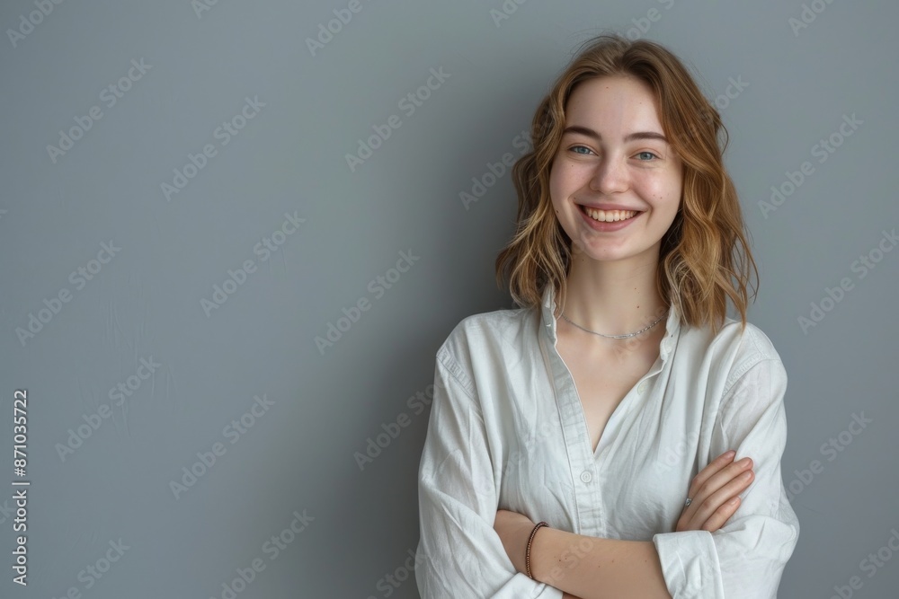 A young woman with blonde hair smiles confidently, standing with crossed arms against a plain grey background A young woman with blonde hair smiles confidently, standing with crossed arms against a plain grey background