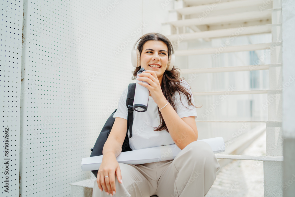 One young caucasian woman student sitting on stairs near university listening to music and drinking coffee One young caucasian woman student sitting on stairs near university listening to music and drinking coffee