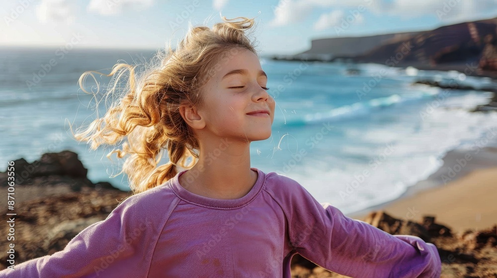 A young girl with blond curly hair is happily embracing the fresh sea breeze on a beautiful beach, with her eyes closed and a peaceful expression on her face. A young girl with blond curly hair is happily embracing the fresh sea breeze on a beautiful beach, with her eyes closed and a peaceful expression on her face.
