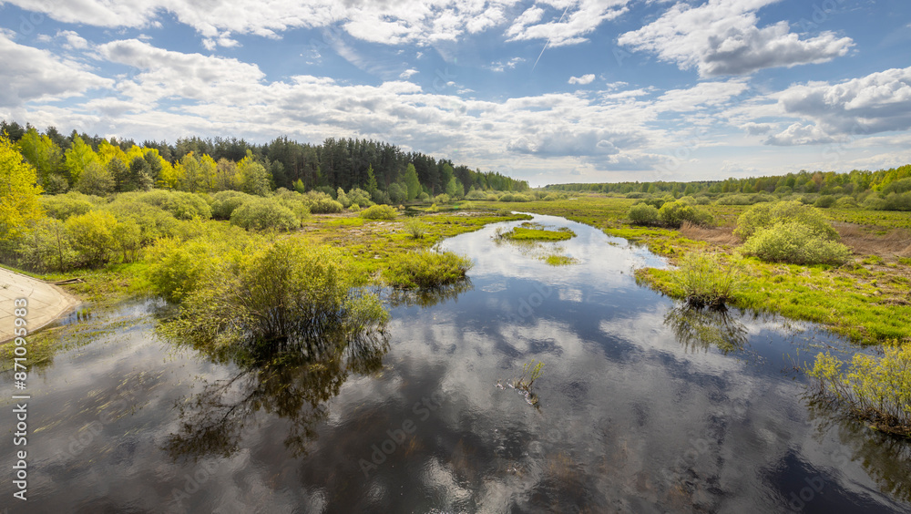 A tranquil river meanders through a verdant landscape, reflecting the bright blue sky and fluffy white clouds. The vibrant greenery of springtime fills the scene. A tranquil river meanders through a verdant landscape, reflecting the bright blue sky and fluffy white clouds. The vibrant greenery of springtime fills the scene.