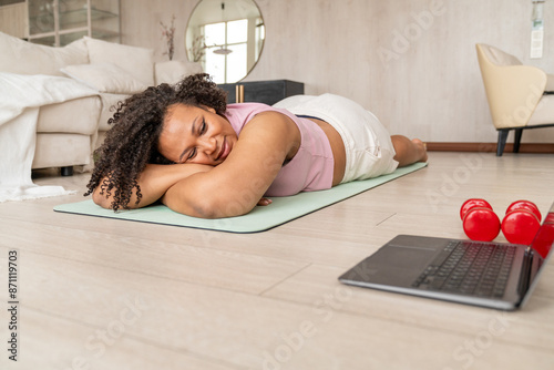 Plus Size Woman Relaxing on Yoga Mat with Dumbbells and Laptop