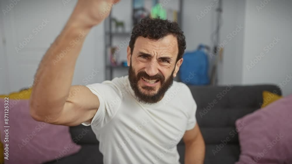 Angry middle-aged man at home, mad and frustrated, in white t-shirt, furiously raises fist with aggressive rage Angry middle-aged man at home, mad and frustrated, in white t-shirt, furiously raises fist with aggressive rage