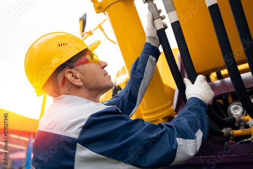 Mechanic repairing hydraulic hose in drilling machine, exploration drilling. Man in hard hat industrial worker. photo