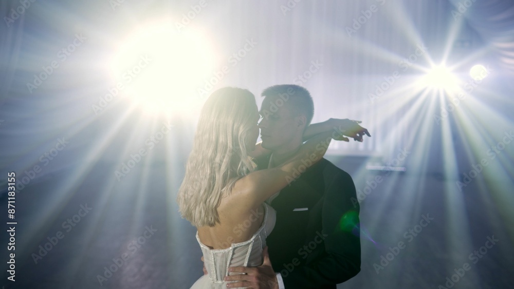Fototapeta premium The bride and groom dance solo under bokeh lights during a wedding ceremony. Stylish groom and happy bride dance the first dance. A couple of bride and groom are dancing under the lights.