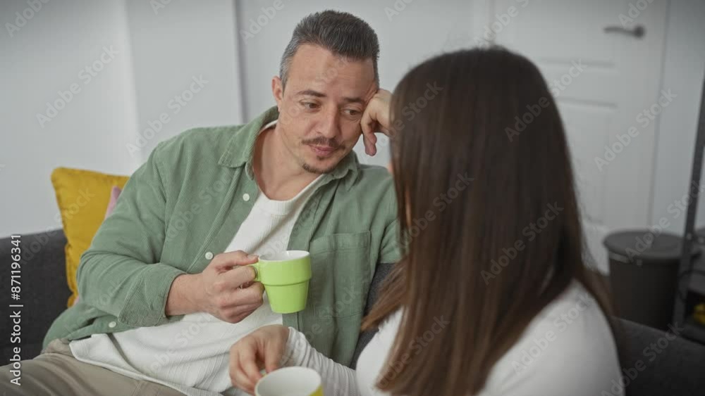 A man and woman share a conversational moment with mugs, conveying togetherness in a cozy living room setting.