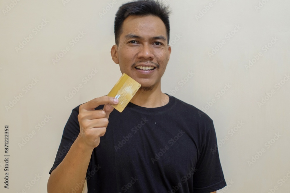 Impressed a Southeast asian man holds in hand debit credit card happy open mouth isolated on yellow color background. Close up of big bank card in hand, finance. Impressed a Southeast asian man holds in hand debit credit card happy open mouth isolated on yellow color background. Close up of big bank card in hand, finance.