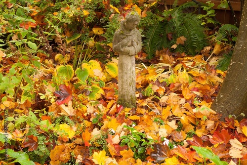 Garden statue of St Francis of Assisi holding a bird, surrounded by colorful autumn leaves