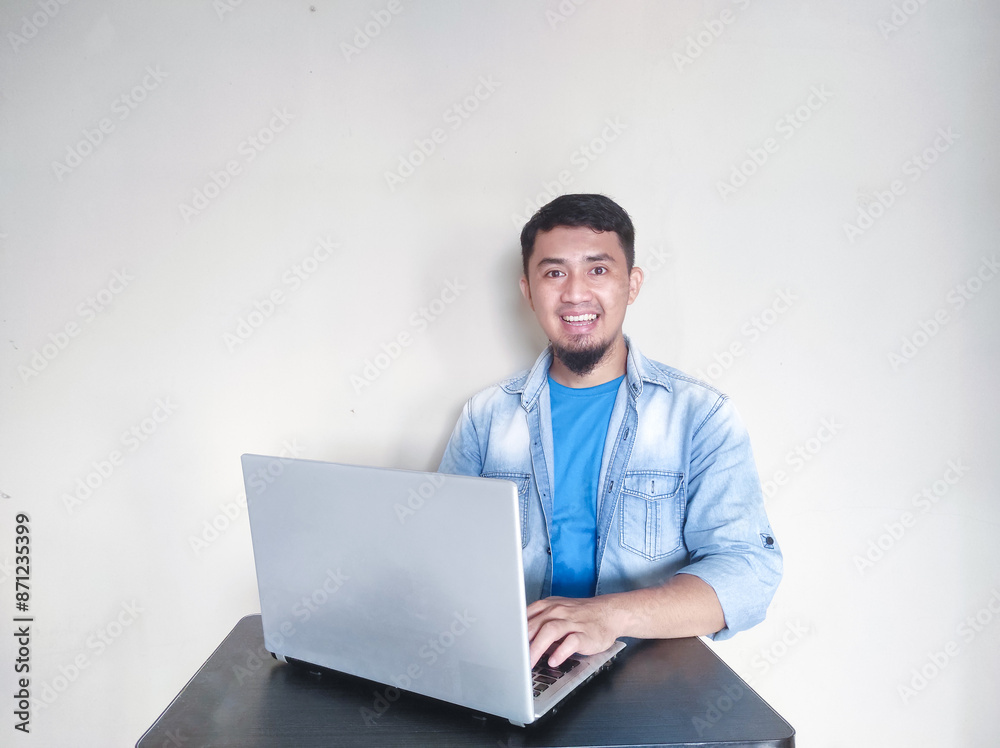 Adult Asian man smiling at camera while using his laptop