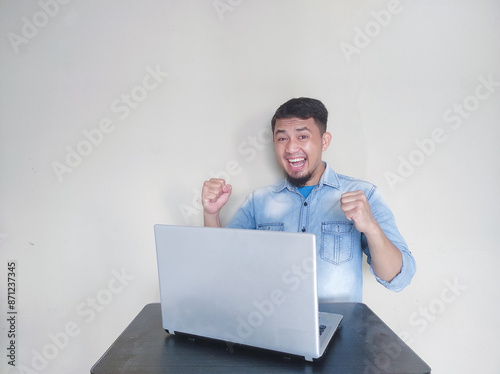 A man at work looks at his laptop with an excited expression while raising and clenching his fists photo