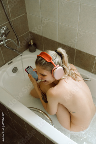 Nude lady sitting in bathtub with headphones and watching music video photo