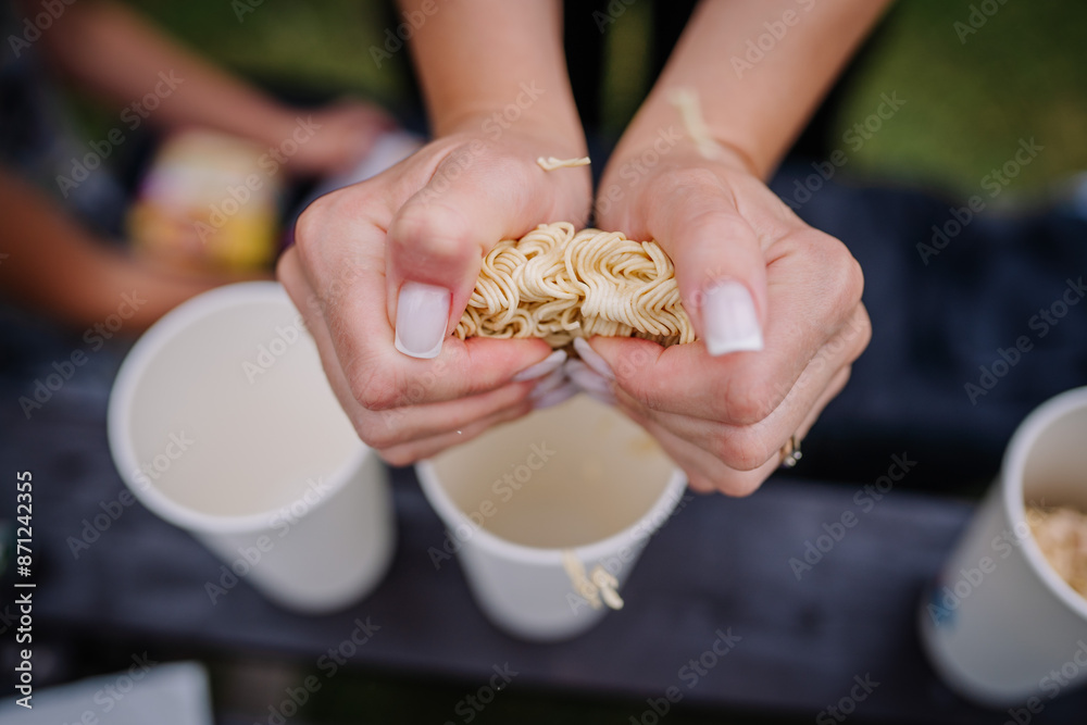 limbazi, Latvia, June 29, 2024 - Close-up of hands breaking instant noodles over paper cups, ready for preparation, outdoor setting with blurred background. limbazi, Latvia, June 29, 2024 - Close-up of hands breaking instant noodles over paper cups, ready for preparation, outdoor setting with blurred background.