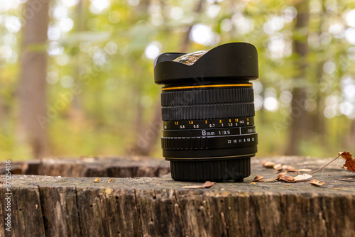 Camera lens resting on weathered wooden surface - surrounded by autumn leaves - blurred forest background. Taken in Toronto, Canada.