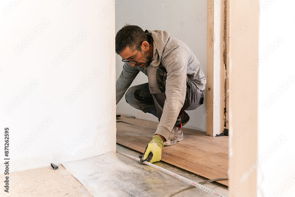 Focused carpenter measuring with tape on floor