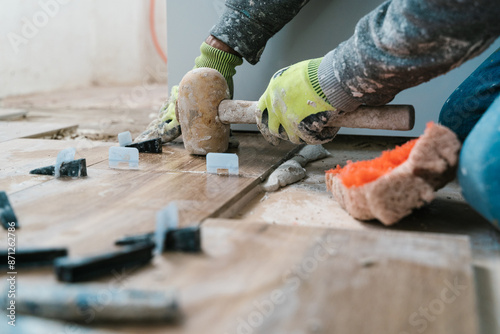 Anonymous repairman laying tiles on floor with rubber mallet photo