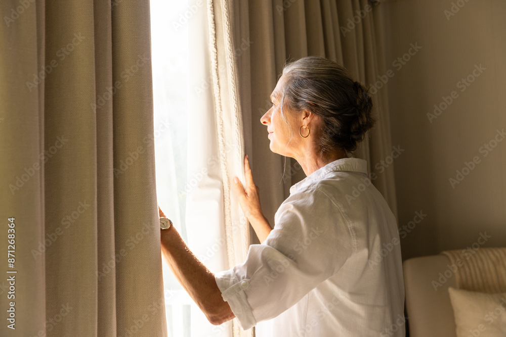 Looking out window, mature woman in white shirt enjoying sunlight at home, copy space Looking out window, mature woman in white shirt enjoying sunlight at home, copy space