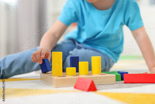 Little boy playing with set of wooden geometric figures on carpet, closeup. Kindergarten activities for motor skills development