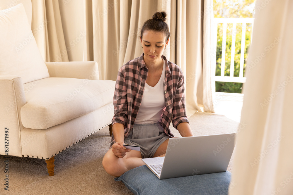 Naklejka premium Sitting on floor, woman using laptop and holding credit card for online shopping