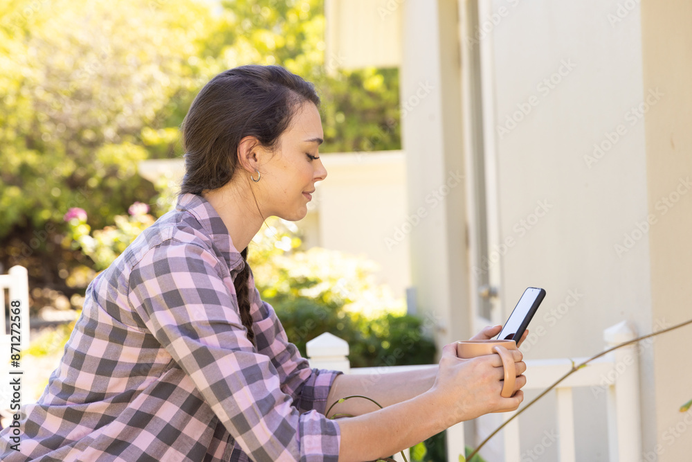 Using smartphone, young woman sitting outside home, enjoying sunny day Using smartphone, young woman sitting outside home, enjoying sunny day