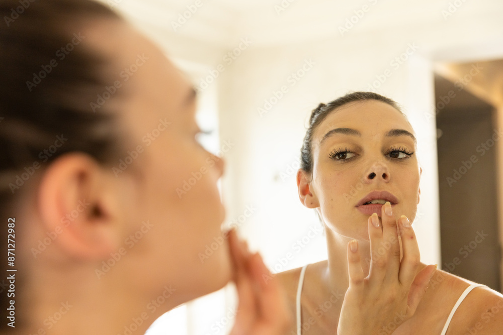 Applying makeup, young woman looking at reflection in bathroom mirror Applying makeup, young woman looking at reflection in bathroom mirror