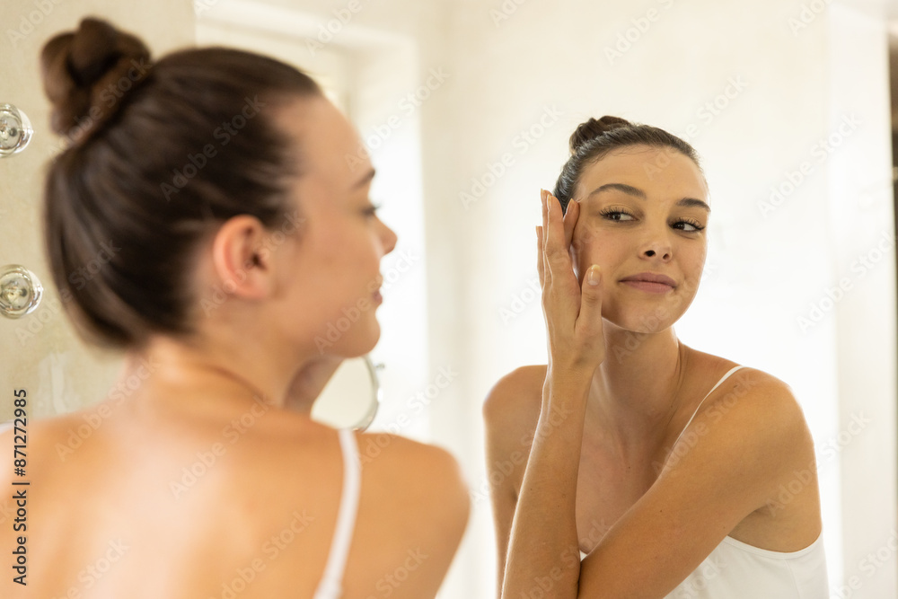 Applying skincare, woman looking in mirror and touching face in bathroom Applying skincare, woman looking in mirror and touching face in bathroom