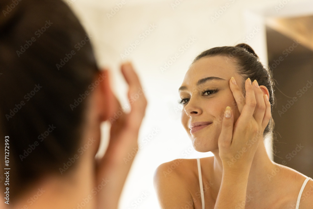 Applying skincare, young woman looking in mirror and smiling at home Applying skincare, young woman looking in mirror and smiling at home