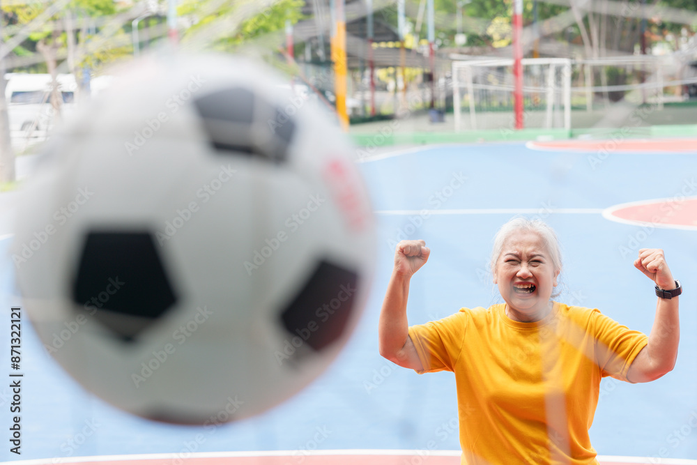 Fototapeta premium Active senior woman playing football in the urban outdoor court, Asian senior woman with a soccer ball, healthy life concepts